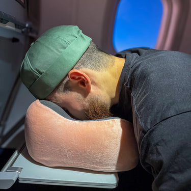 Coussin de voyage en velours rose utilisé sur une table dans un avion, offrant un soutien ergonomique pour le cou et un confort optimal grâce à sa mousse à mémoire de forme.